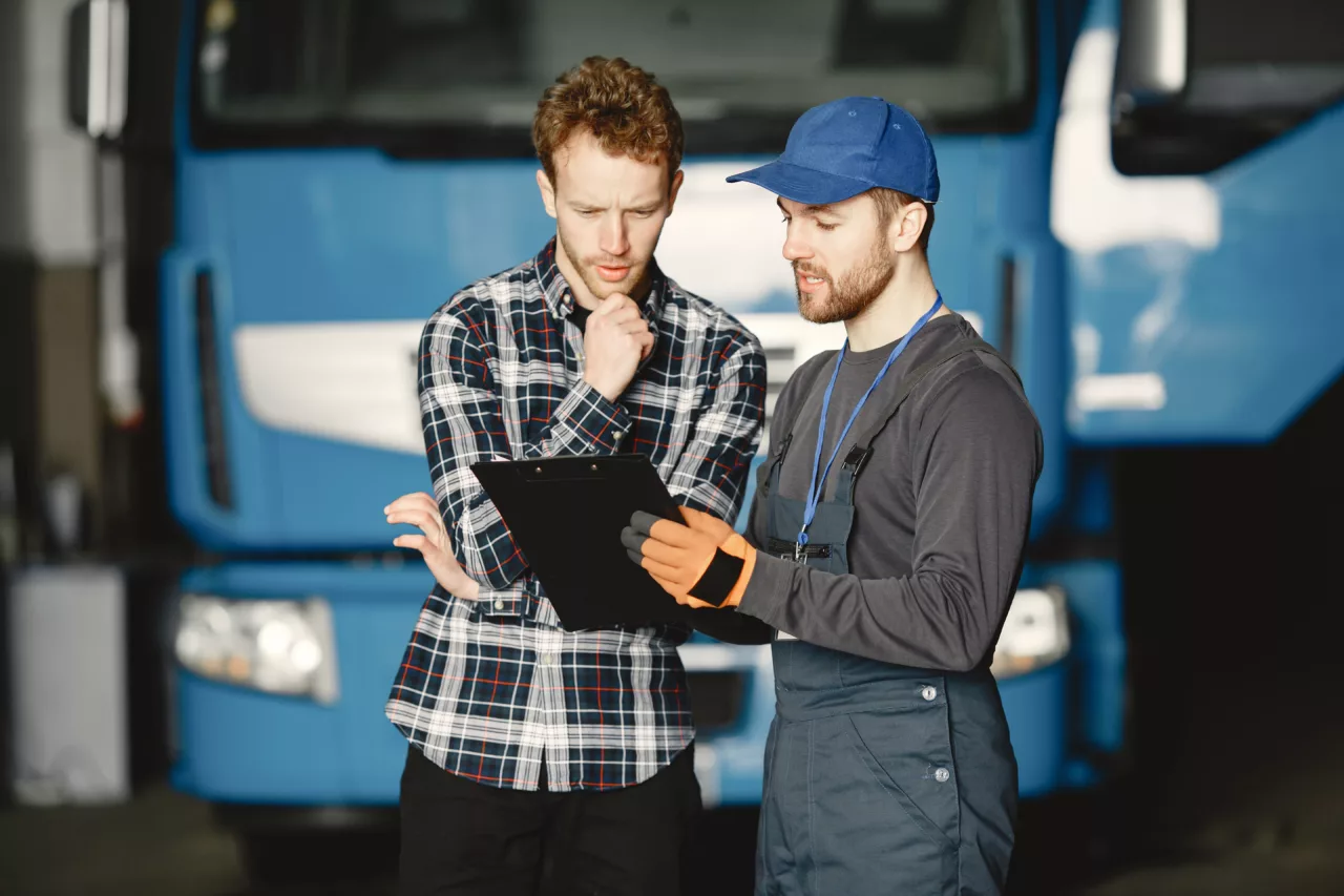 Twee mannen voor een vrachtwagen die naar een clipboard kijken